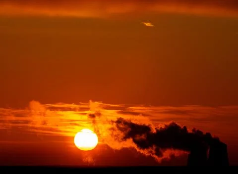 Dramatic black smoke with orange dawn sky with the rising sun. Stock Photos
