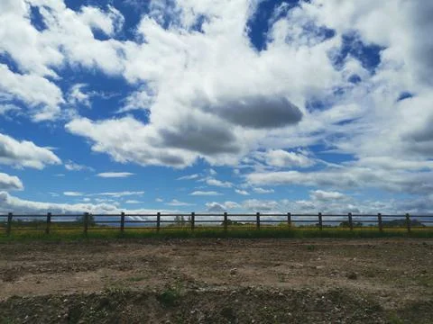 Dramatic blue and white cloudy sky above rough ground and wooden fence Stock Photos