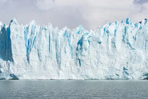 Dramatic Blue Ice Glacier Wall Rise from Water Under Cloudy Sky Argentina Stock Photos