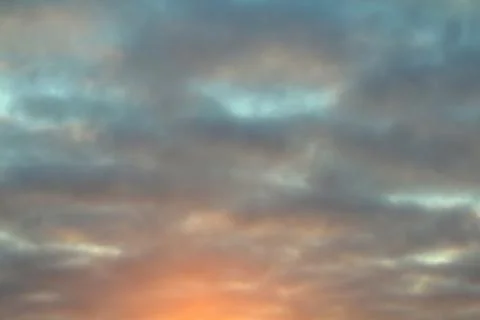 Dramatic blue sky with clouds backlit by the sun at dusk. Stock Photos