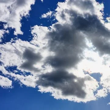 Dramatic blue sky with dark and white fluffy clouds and sunlight Stock Photos