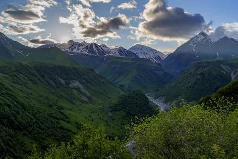 Dramatic Caucasus mountain valley at sunset with snow capped peaks Stock Photos
