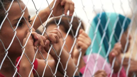 Dramatic children's eyes and hands through the fence in a refugee camp. Mosul Stock Footage 158379489