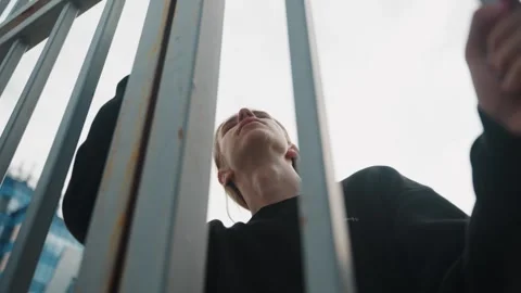 Dramatic cityscape capturing man behind gates looking upward. Suspenseful urban Stock Footage 334946368