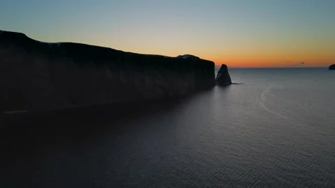 Dramatic cliff face and sea stack bathed in twilight glow aerial drone footag Stock Footage 337278931