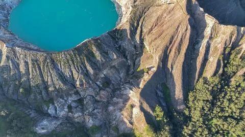 Dramatic cliff textures frame Kelimutu mystical blue lake, highlighting the i Stock Photos
