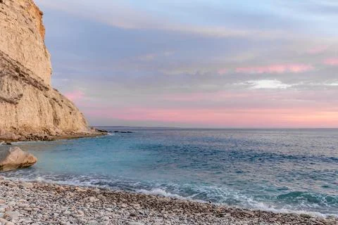 Dramatic cliffs meet the gentle waves at twilight, a lonely rock standing sen Foto stock
