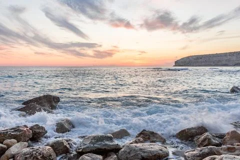 Dramatic cliffs meet the gentle waves at twilight, a lonely rock standing sen Stock Photos