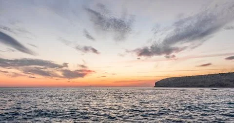 Dramatic cliffs meet the gentle waves at twilight, a lonely rock standing sen Stock Photos