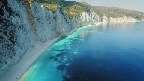 Dramatic cliffs meeting blue Ionian Sea along white pebble beach in Kefalonia Stock Footage 312653999