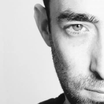 Dramatic closeup portrait of a young bearded man half expressionless face on  Stock Photos