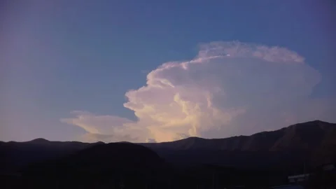 Dramatic cloud formation glowing in warm sunlight above dark mountain silhouette Stock Footage 340579722