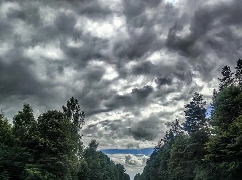 Dramatic cloud formations over a tree-lined road in a rural landscape 写真素材