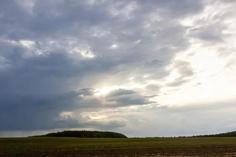 Dramatic cloud formations over a vast field at dusk create an atmospheric l.. Stock Photos