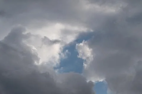 Dramatic cloud opening reveals sky center, sharp gray walls frame small blu.. Foto stock