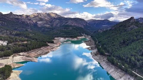 Dramatic cloud shadows over tranquil turquoise waters surrounded by pinecov.. Stock Photos