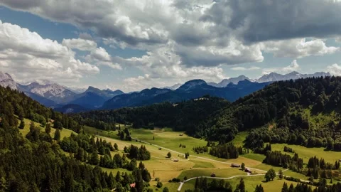 Dramatic cloud timelapse over green alpine fields, forest and mountain peaks in Video stock 340827092