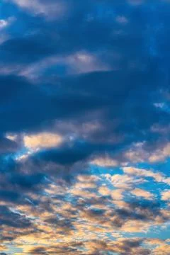 Dramatic clouds in blue sky, illuminated by rays of sun at colorful sunset to Stock Photos