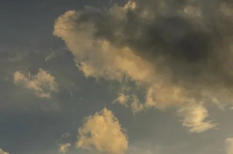 Dramatic clouds dance in the evening sky, casting shades of gold and gray o.. Stock Photos