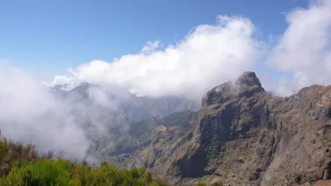 Dramatic clouds drifting across rugged volcanic mountain peaks under a blue sky Видео 345840185