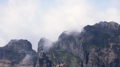 Dramatic clouds drifting across rugged volcanic mountain peaks under a blue sky Stock Footage 346247089