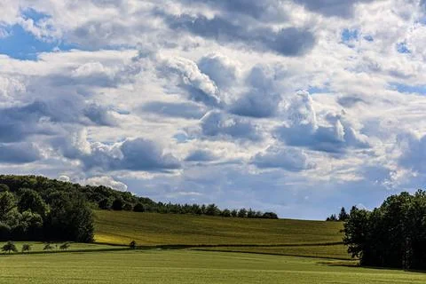Dramatic clouds gather over a lush green rolling landscape with fields and .. Foto stock