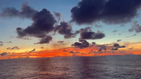 Dramatic clouds gather over a vast ocean during a vibrant sunset with hues .. Stock Footage 338282853
