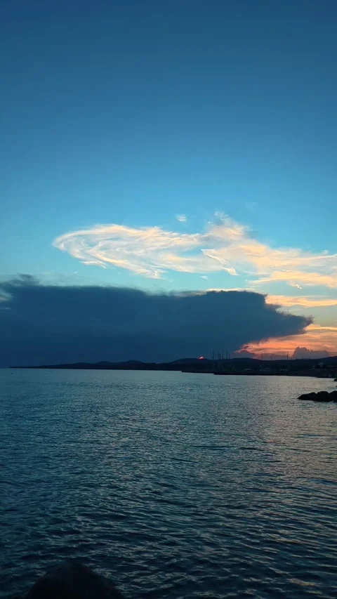Dramatic clouds glow above calm blue waters. Trani Ammouda, Greece. Vertical Stock Footage 339630356