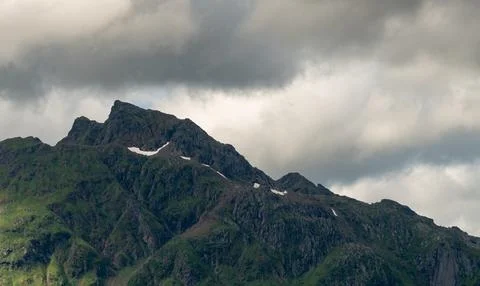 Dramatic clouds hovering over green mountain peaks with patches of snow Stock Photos