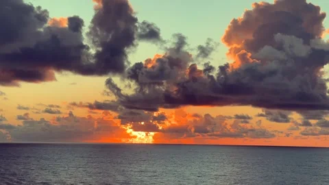 Dramatic clouds light up the sky over a calm ocean at sunset 動画素材 338282765