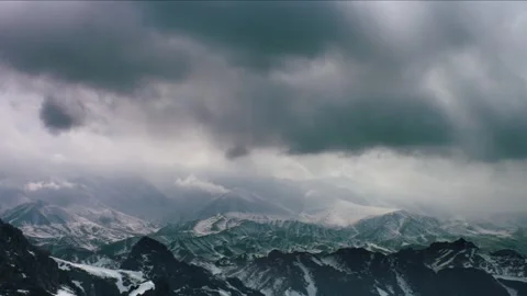 Dramatic clouds move over snow-covered mountains, sun rays piercing through.. Vidéo 344995982
