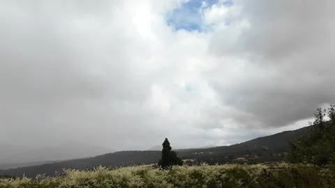 Dramatic clouds moving fast over a rural mountain landscape with a lone cypress  Stock Footage 343781733