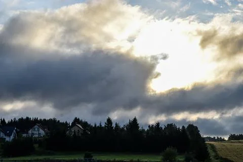 Dramatic clouds obscure the sun over a rural landscape with houses 库存照片