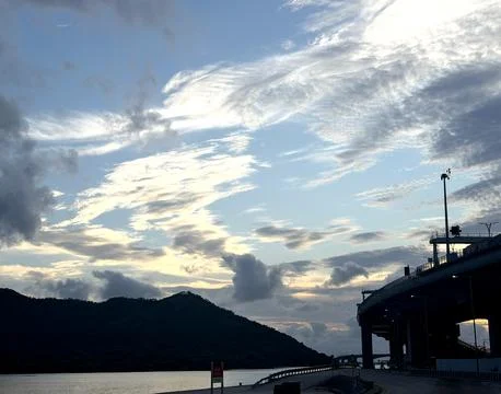 Dramatic clouds over a coastal highway and silhouetted island at dusk Stock Photos
