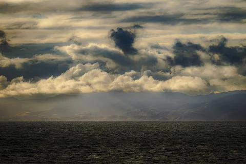Dramatic clouds over the ocean and distant mountains at sunset Photos