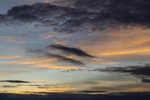Dramatic clouds painting the sky at sunset with golden hues and dark formatio Stock Photos