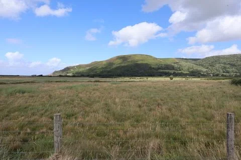 Dramatic clouds on a rounded hill stand behind a field of crops on Porlock sa Foto stock