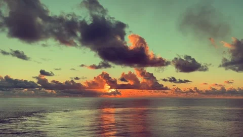 Dramatic clouds scatter across the sky as the sun sets over a calm ocean cr.. Stock Footage 338281820