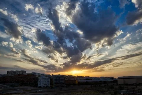 Dramatic clouds show up as the sun sets behind the buildings. 写真素材