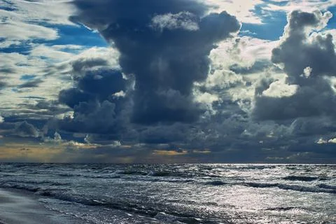 Dramatic clouds in the sky above the glittering sea waves Stock Photos