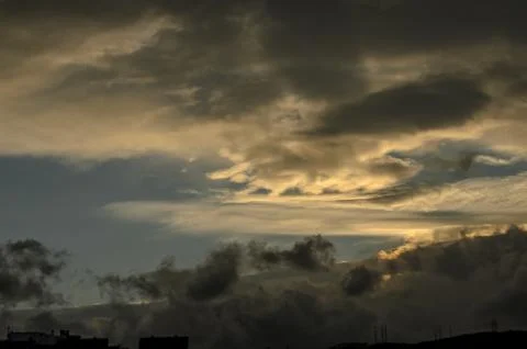 Dramatic clouds swirl in twilight, casting shadows over the horizon as dusk.. Stockfoto's