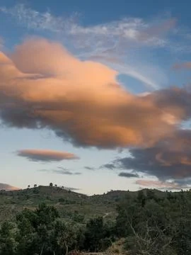Dramatic cloudscape glows at sunset over green hills and trees Stock Photos