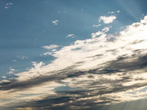 Dramatic cloudscape with layered sunlit clouds and soft rays across a blue Photos