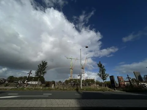 Dramatic cloudscape over urban riverside with construction cranes, faint Stock Photos