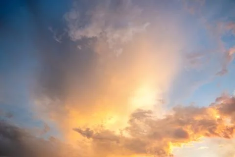 Dramatic cloudscape with puffy clouds lit by orange setting sun and blue sky. Stock Photos