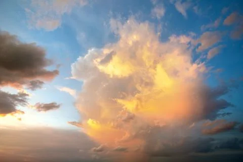 Dramatic cloudscape with puffy clouds lit by orange setting sun and blue sky. Stock Photos