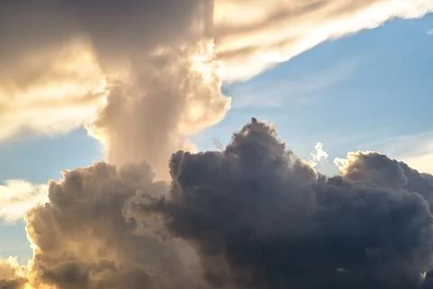 Dramatic cloudscape with puffy clouds lit by orange setting sun and blue sky. Stock Photos