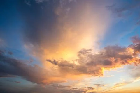Dramatic cloudscape with puffy clouds lit by orange setting sun and blue sky. Stock Photos
