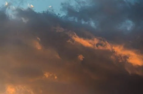 Dramatic cloudscape scene at orange sunset, colored sun lights on the blue sk Stock Photos