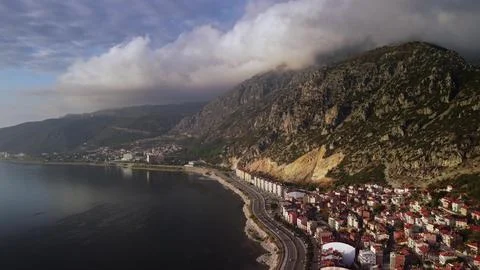 Dramatic cloudwrapped mountain looming over coastal town built along the sea Stock Photos